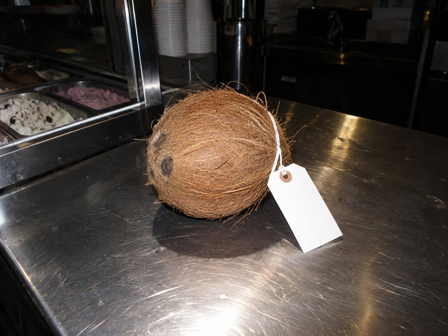 Un coco entero con una etiqueta de evidencia en blanco, sobre el mostrador de acero de una heladería, fotografiado con flash